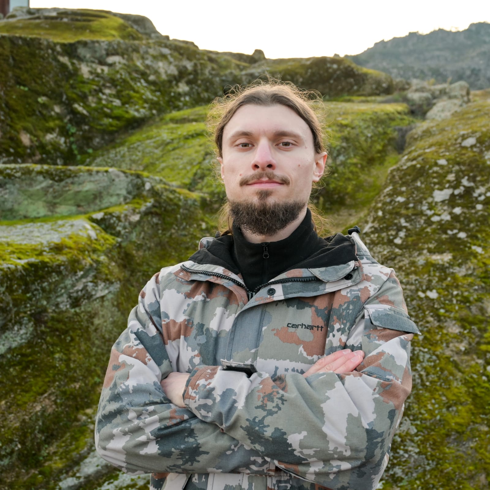Ricardo Tito, founder and guide of PortusQuest, standing with arms folded among moss-covered granite boulders